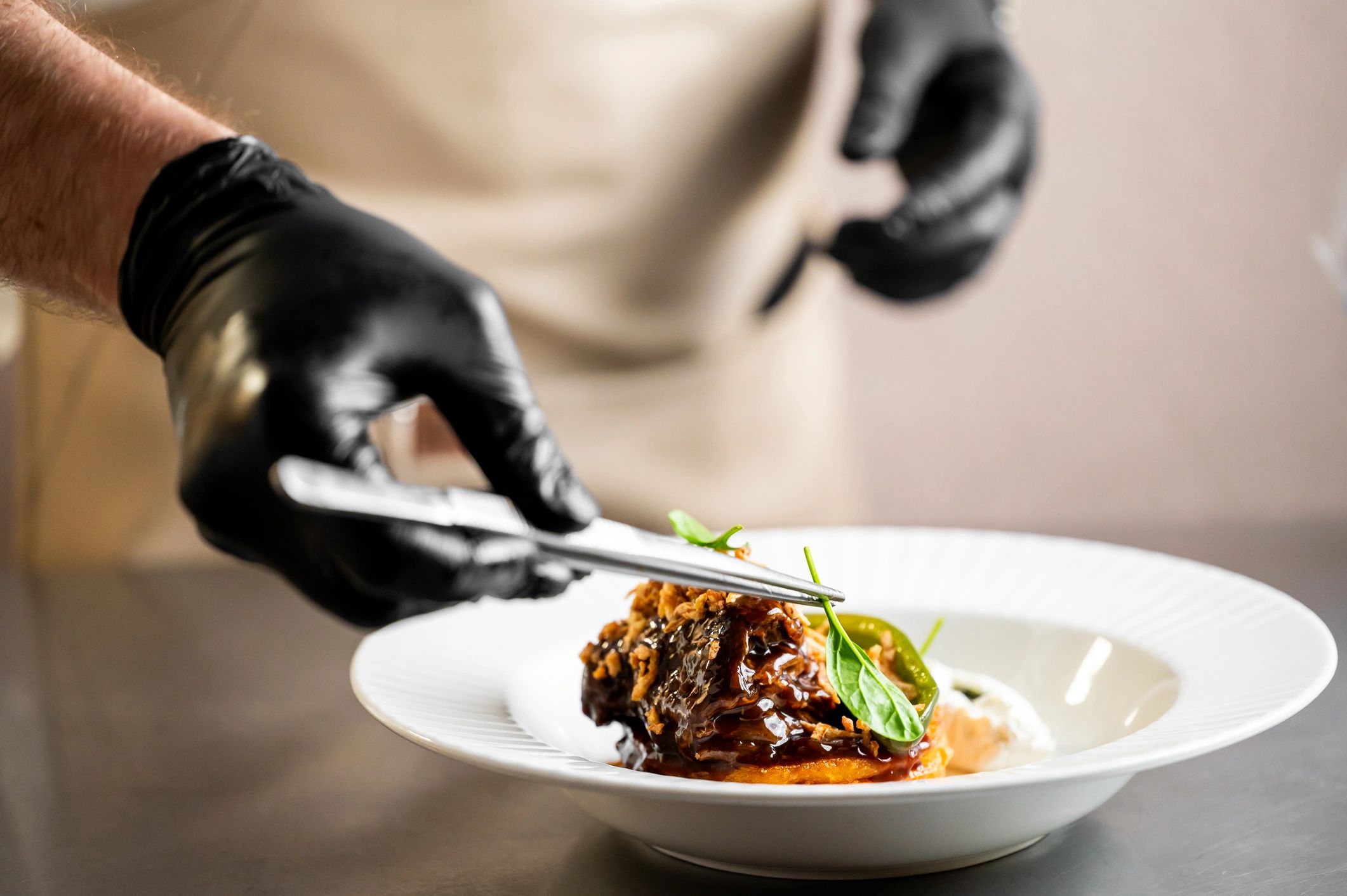 Chef plating a gourmet dish with tweezers in a professional kitchen